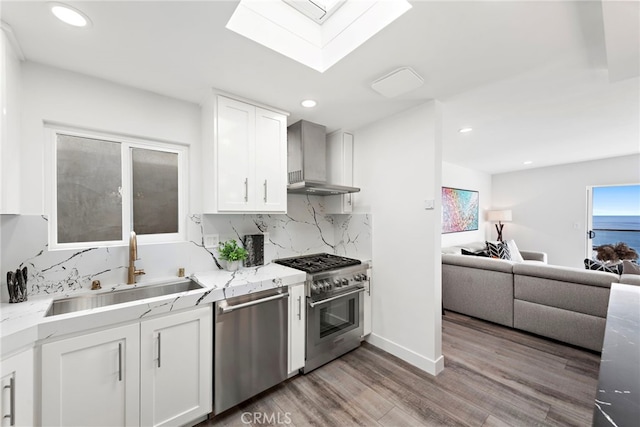 kitchen featuring sink, stainless steel appliances, tasteful backsplash, white cabinets, and wall chimney exhaust hood