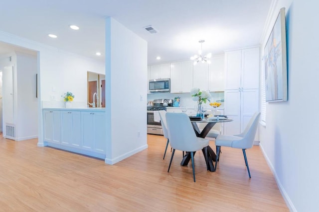 dining room with ornamental molding, sink, a notable chandelier, and light hardwood / wood-style floors