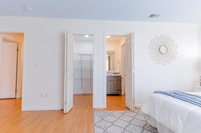 bedroom featuring crown molding, a walk in closet, light hardwood / wood-style floors, and a closet