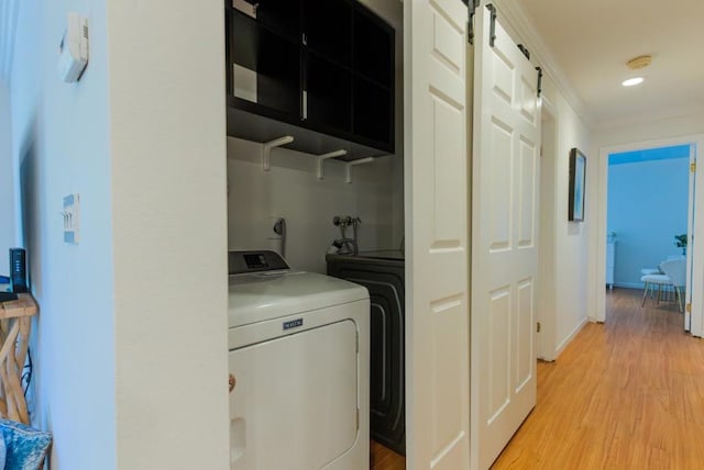 laundry room featuring a barn door, ornamental molding, separate washer and dryer, and light hardwood / wood-style floors