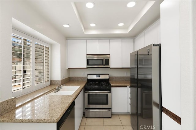 kitchen with appliances with stainless steel finishes, white cabinetry, sink, light tile patterned floors, and a raised ceiling