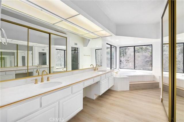 bathroom with a relaxing tiled tub, vanity, and wood-type flooring