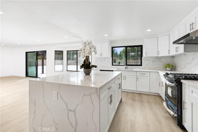 kitchen with light stone counters, white cabinetry, gas range oven, and backsplash