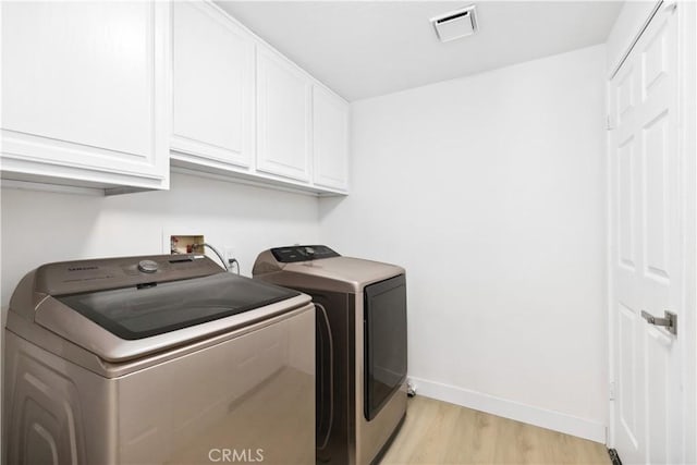 washroom featuring cabinets, washing machine and clothes dryer, and light hardwood / wood-style flooring