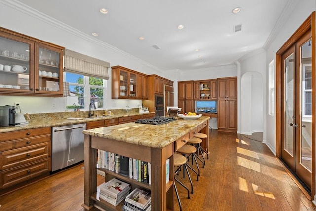 kitchen featuring dark wood-type flooring, crown molding, appliances with stainless steel finishes, a kitchen island, and light stone countertops