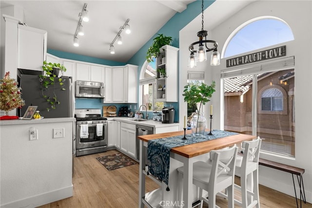 kitchen featuring butcher block counters, white cabinetry, decorative light fixtures, vaulted ceiling, and appliances with stainless steel finishes