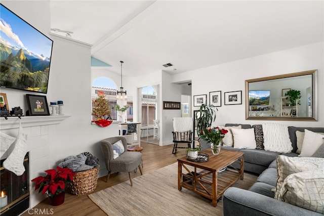 living room with a tiled fireplace, vaulted ceiling with beams, hardwood / wood-style floors, and a notable chandelier