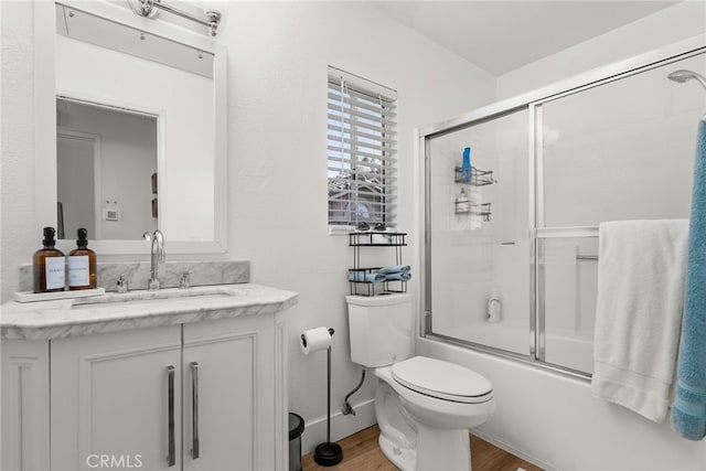 full bathroom featuring vanity, toilet, hardwood / wood-style floors, and bath / shower combo with glass door