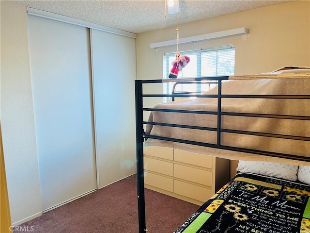 unfurnished bedroom with dark carpet, a textured ceiling, a closet, and ceiling fan