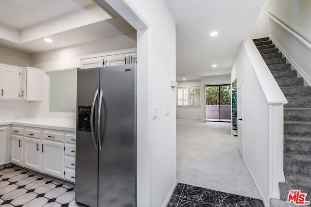 kitchen with stainless steel fridge with ice dispenser, light colored carpet, and white cabinets