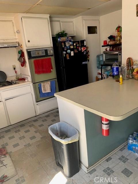 kitchen featuring cooktop, light countertops, white cabinets, a peninsula, and freestanding refrigerator
