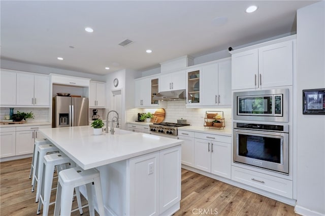 kitchen with appliances with stainless steel finishes, a breakfast bar, a center island with sink, and white cabinets