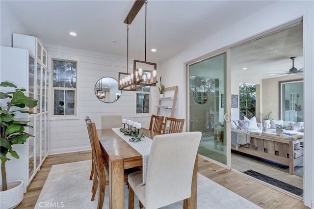 dining space with ceiling fan with notable chandelier and light wood-type flooring