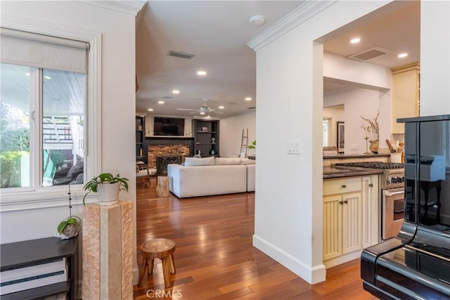 kitchen featuring ceiling fan, cream cabinets, wood-type flooring, ornamental molding, and a brick fireplace