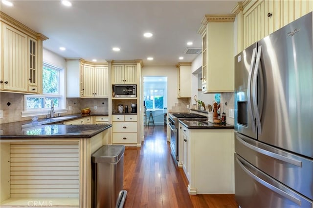 kitchen featuring sink, dark wood-type flooring, stainless steel appliances, decorative backsplash, and cream cabinetry