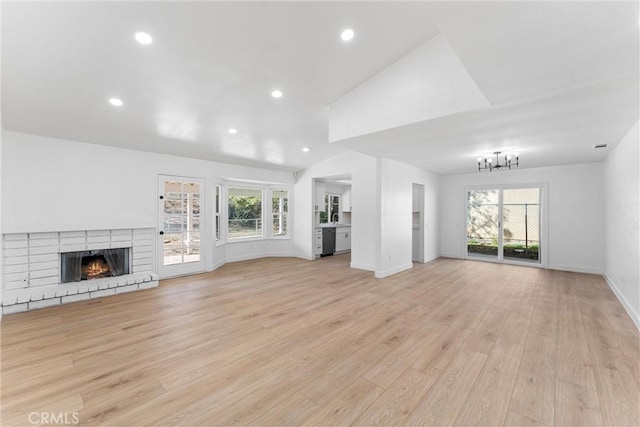 unfurnished living room featuring an inviting chandelier, a brick fireplace, light hardwood / wood-style floors, and a healthy amount of sunlight