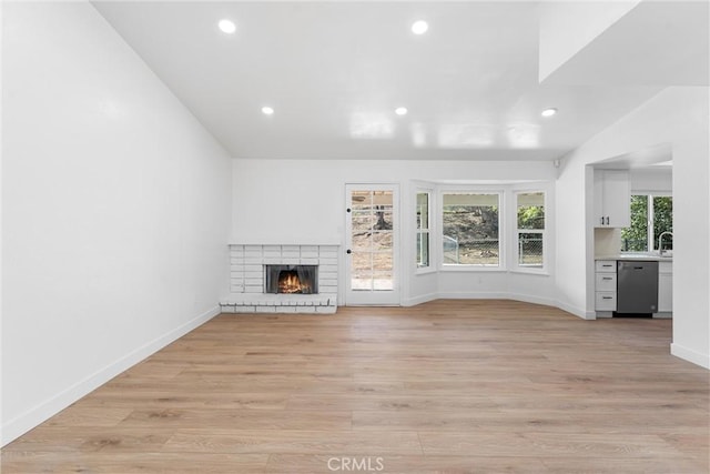 unfurnished living room with sink, light hardwood / wood-style floors, and a brick fireplace