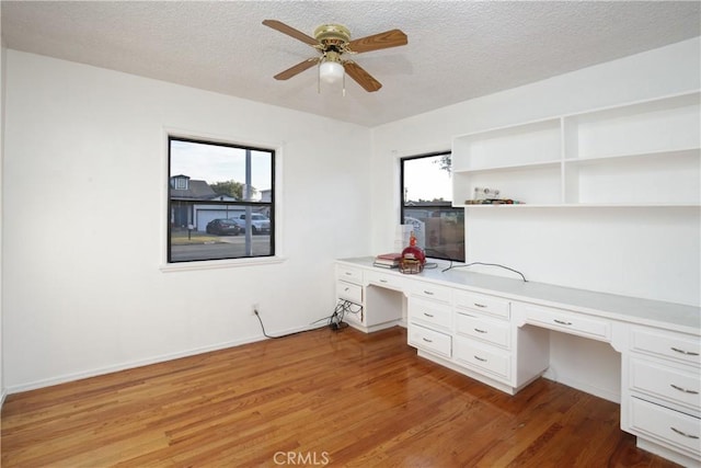 unfurnished office featuring ceiling fan, built in desk, a textured ceiling, and light hardwood / wood-style floors