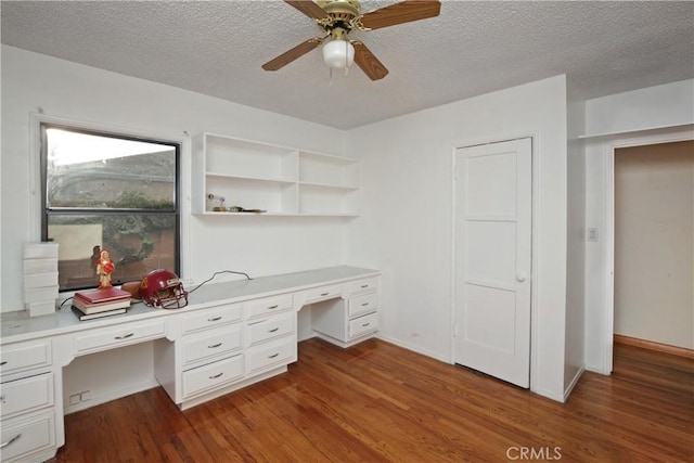 unfurnished office featuring ceiling fan, dark hardwood / wood-style floors, built in desk, and a textured ceiling