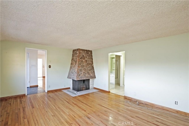 unfurnished living room featuring a stone fireplace, light hardwood / wood-style flooring, and a textured ceiling