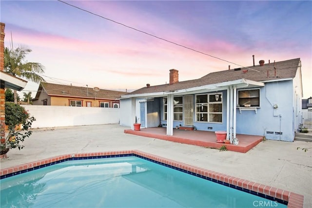 back house at dusk featuring a fenced in pool and a patio area