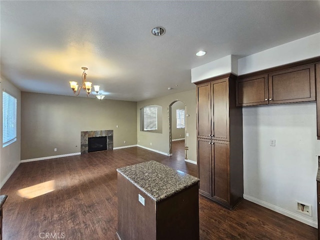 kitchen featuring dark brown cabinetry, a fireplace, light stone countertops, dark hardwood / wood-style flooring, and a chandelier