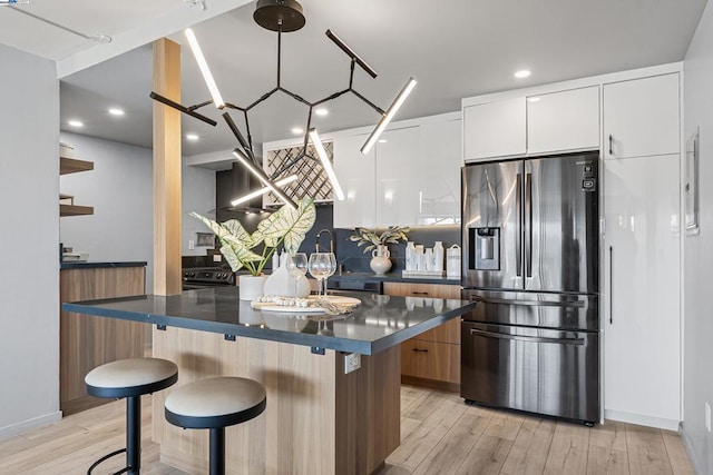 kitchen with a kitchen breakfast bar, stainless steel refrigerator with ice dispenser, white cabinets, a kitchen island, and light wood-type flooring