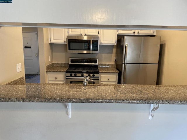 kitchen with a kitchen bar, white cabinetry, appliances with stainless steel finishes, kitchen peninsula, and dark stone counters