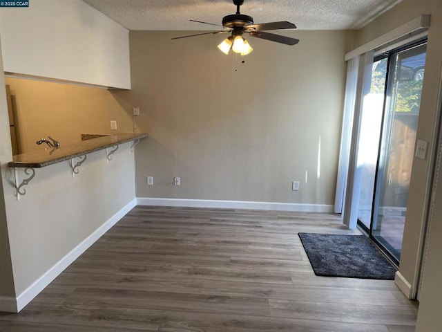 unfurnished dining area featuring dark wood-type flooring, ceiling fan, and a textured ceiling