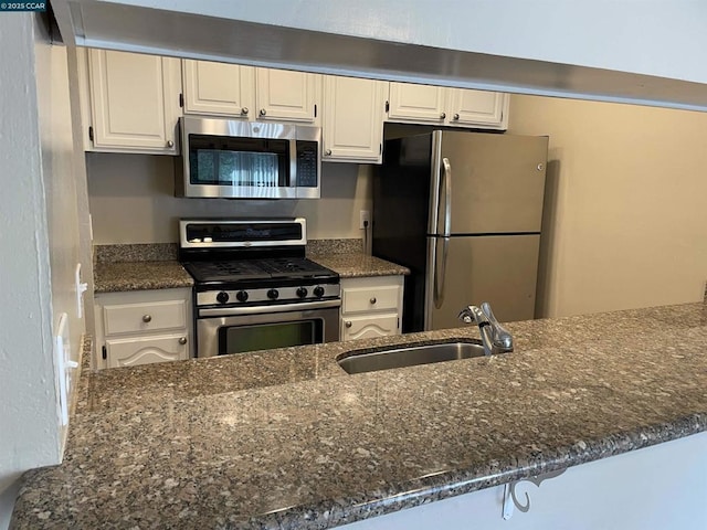 kitchen featuring sink, white cabinetry, dark stone countertops, kitchen peninsula, and stainless steel appliances