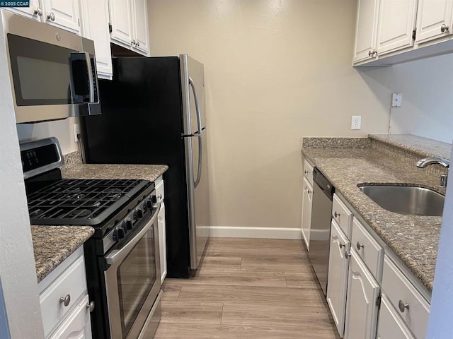 kitchen featuring sink, light hardwood / wood-style flooring, dark stone countertops, stainless steel appliances, and white cabinets