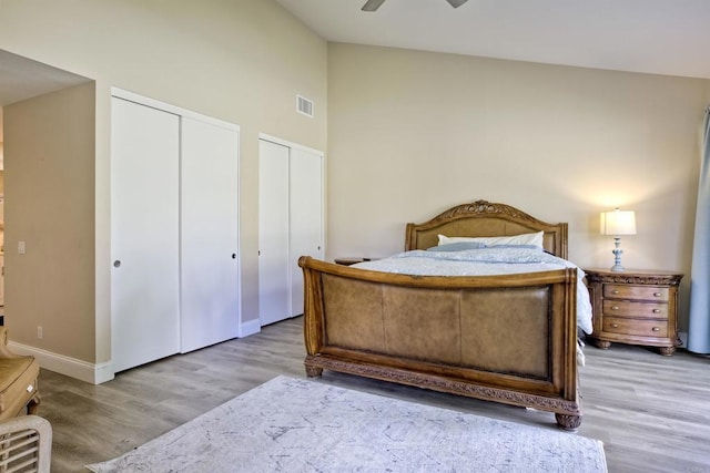 bedroom featuring ceiling fan, light hardwood / wood-style flooring, multiple closets, and vaulted ceiling