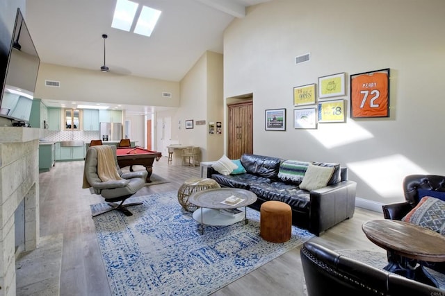 living room featuring a skylight, high vaulted ceiling, light hardwood / wood-style floors, and beamed ceiling