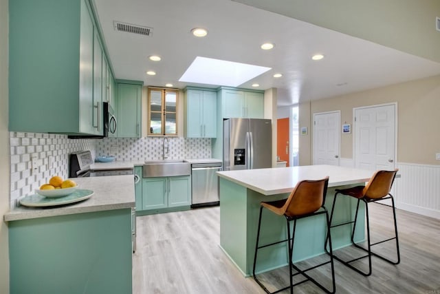 kitchen with appliances with stainless steel finishes, a skylight, sink, a kitchen breakfast bar, and a center island