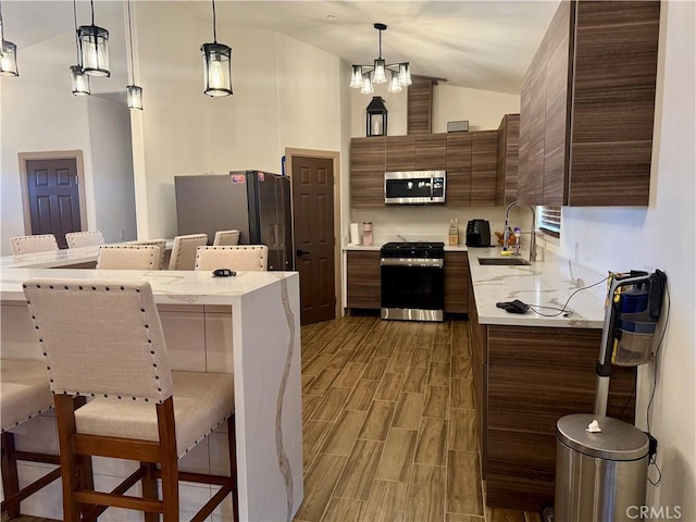 kitchen with pendant lighting, lofted ceiling, sink, a breakfast bar area, and stainless steel appliances