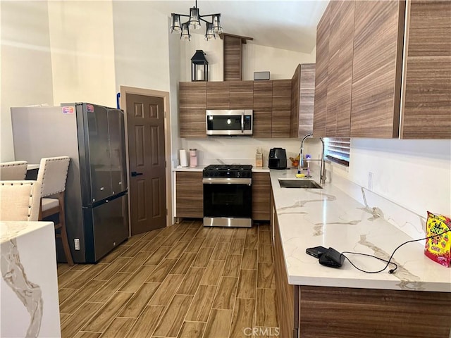 kitchen featuring lofted ceiling, sink, appliances with stainless steel finishes, hanging light fixtures, and light stone countertops