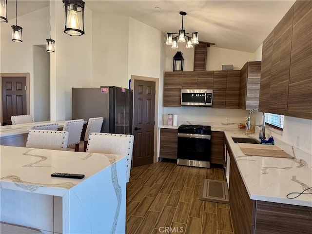 kitchen featuring appliances with stainless steel finishes, light stone countertops, decorative light fixtures, high vaulted ceiling, and sink