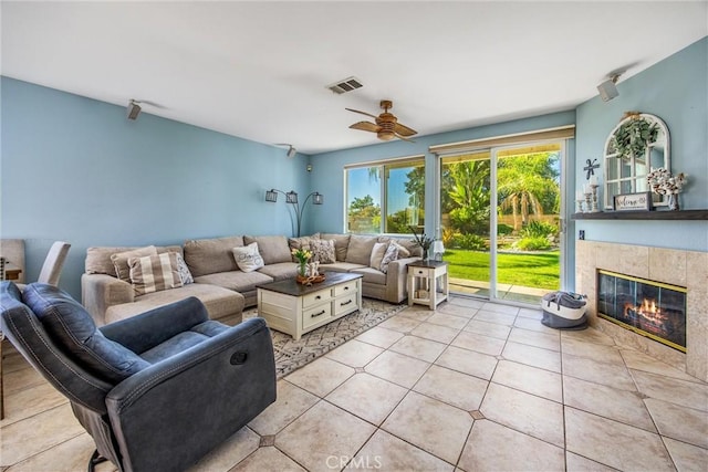 living room featuring a tiled fireplace, ceiling fan, and light tile patterned flooring