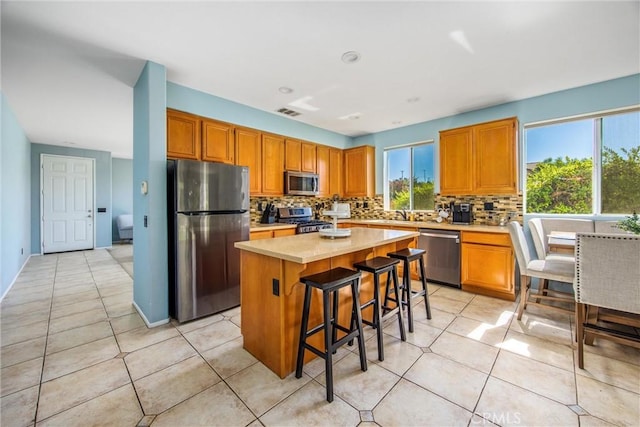 kitchen with light tile patterned floors, appliances with stainless steel finishes, a kitchen breakfast bar, a center island, and tasteful backsplash