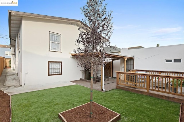 rear view of property with a wooden deck, a lawn, and a patio