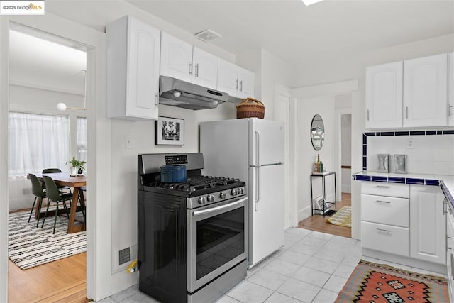 kitchen featuring light tile patterned floors, white cabinetry, tasteful backsplash, tile counters, and gas stove