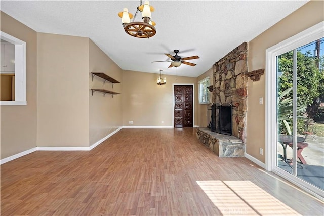 unfurnished living room with a stone fireplace, ceiling fan with notable chandelier, wood-type flooring, lofted ceiling, and a textured ceiling