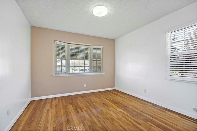 spare room featuring a textured ceiling, wood-type flooring, and a healthy amount of sunlight