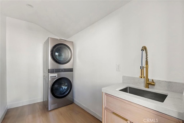 laundry room with stacked washing maching and dryer, sink, and light hardwood / wood-style flooring