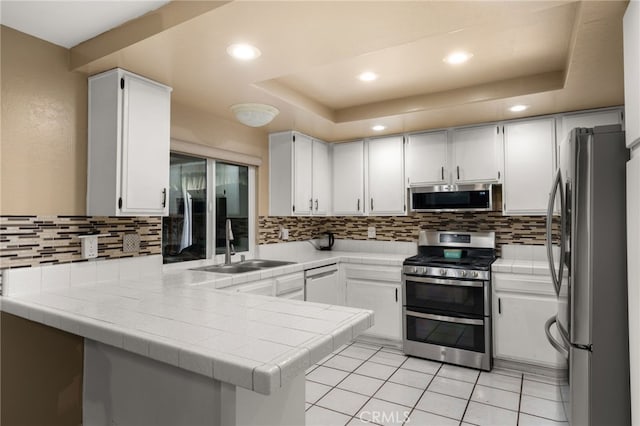 kitchen featuring stainless steel appliances, white cabinetry, a raised ceiling, and kitchen peninsula