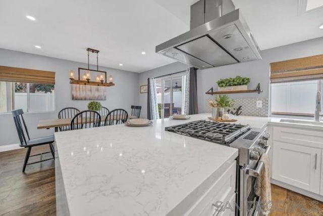 kitchen featuring sink, white cabinetry, island range hood, high end stove, and decorative light fixtures