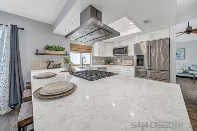 kitchen with white cabinetry, island range hood, light stone countertops, and appliances with stainless steel finishes