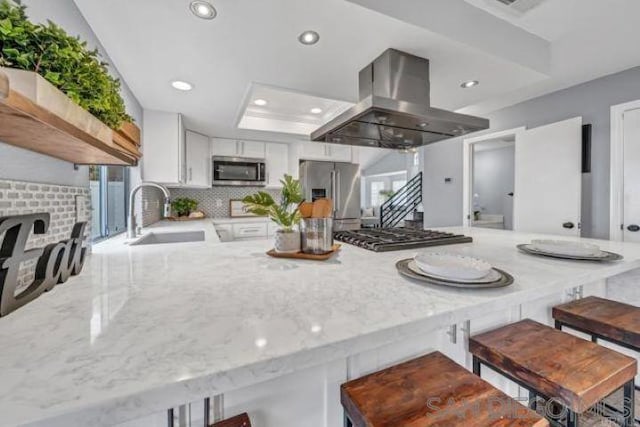 kitchen featuring sink, appliances with stainless steel finishes, kitchen peninsula, island exhaust hood, and white cabinets