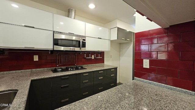 kitchen featuring dark stone countertops, backsplash, black gas cooktop, and white cabinets