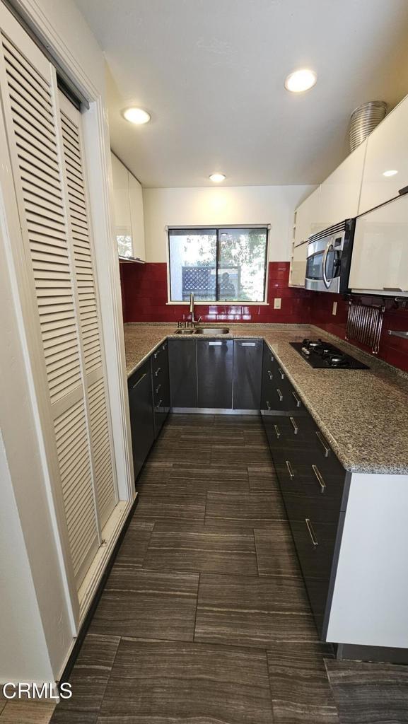 kitchen with white cabinetry, stone countertops, black gas stovetop, and sink